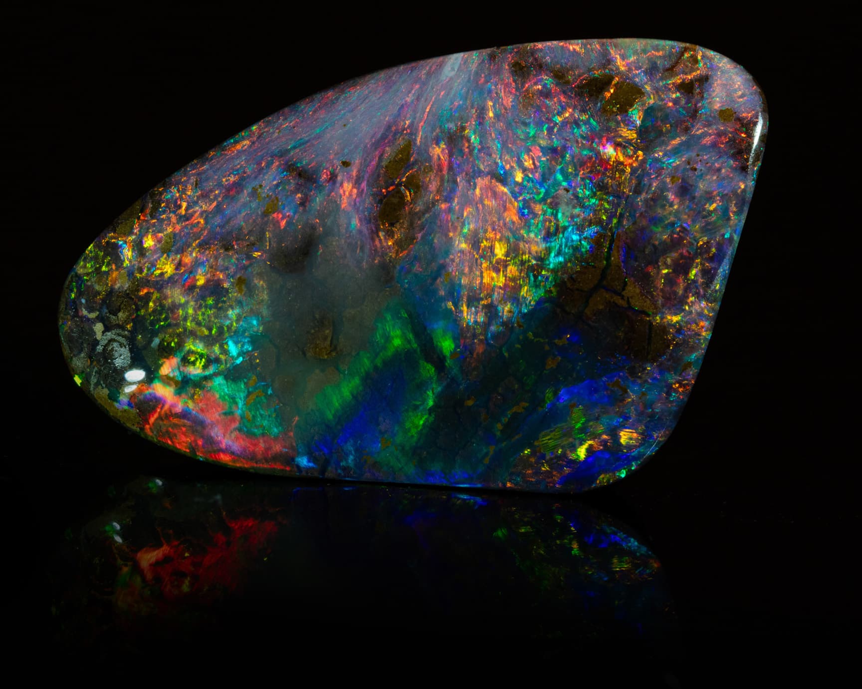 Geschliffener Opal mit buntem Farbspiel vor schwarzem Hintergrund