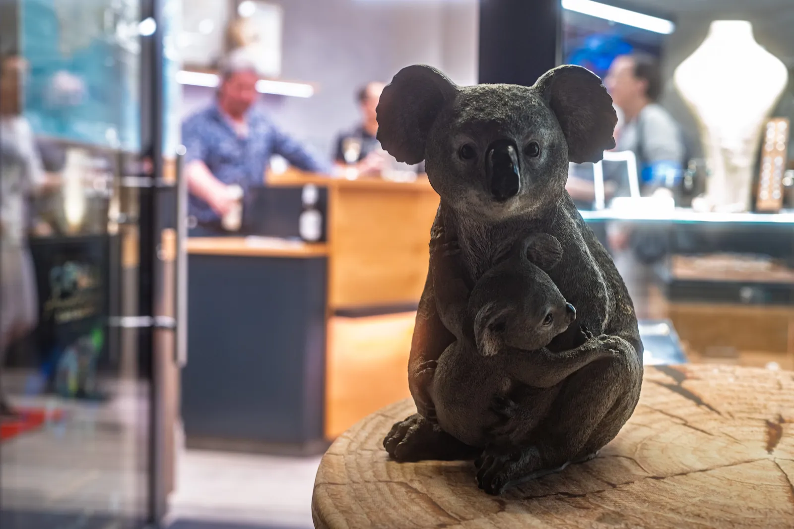 Koala-Figur auf einer Baumscheibe, dahinter Gäste im Verkaufsraum