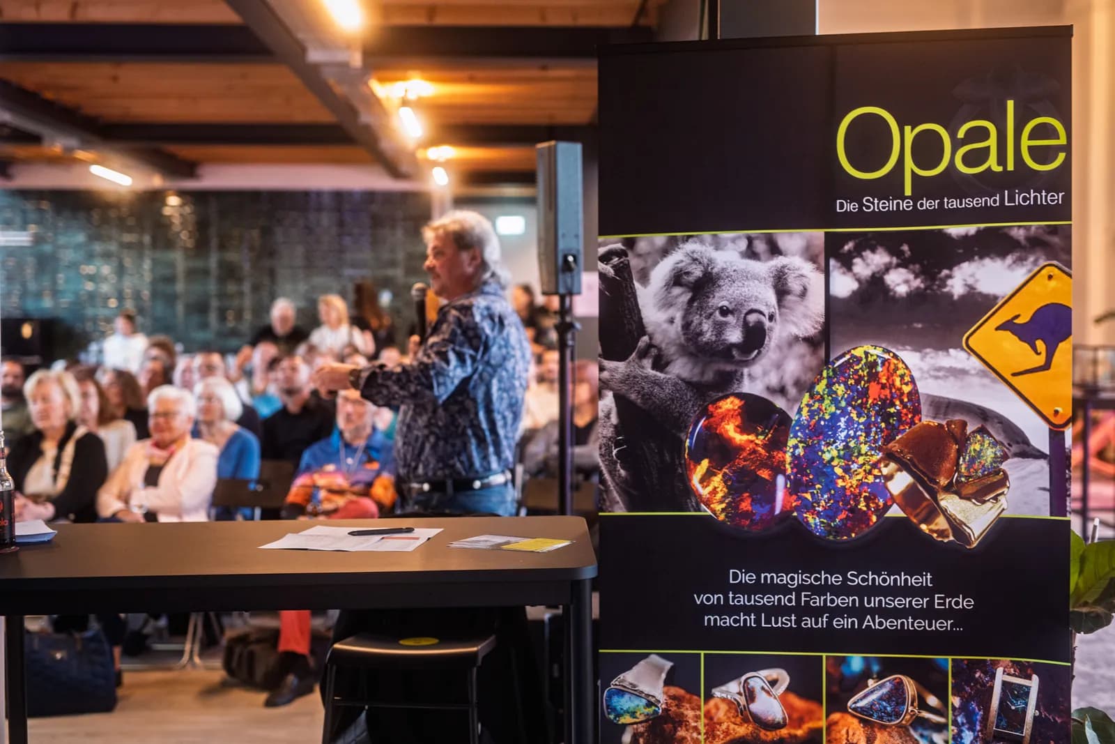 Volles Haus im Postwerk: ein Redner spricht zum Publikum, daneben das Opal-Banner